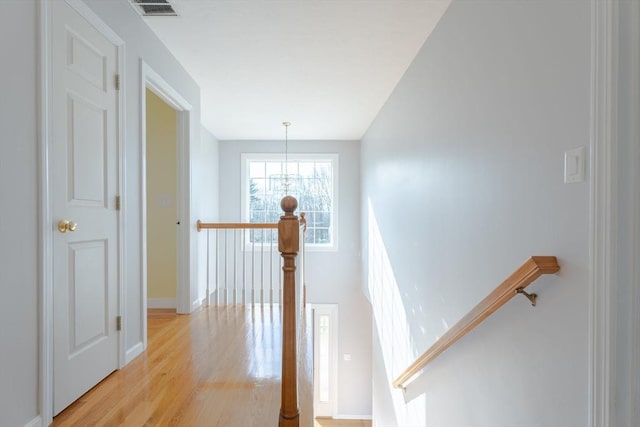 hall featuring visible vents, an upstairs landing, baseboards, and light wood finished floors