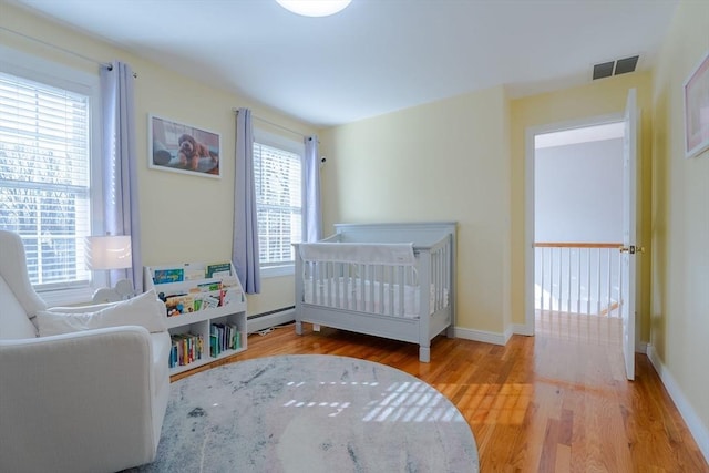 bedroom featuring a baseboard radiator, baseboards, visible vents, and wood finished floors