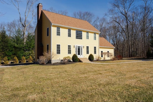 colonial-style house with entry steps, a chimney, a front lawn, and roof with shingles