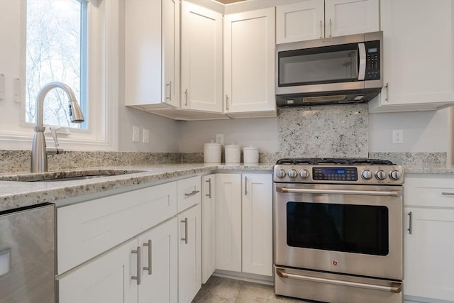 kitchen with a sink, stainless steel appliances, light stone countertops, and white cabinetry