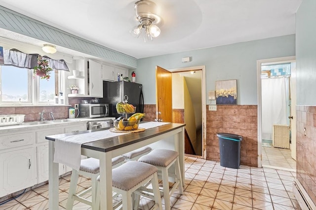 369-371 Mill St, New Bedford, MA 02740 - kitchen featuring stainless steel microwave, a baseboard radiator, a wainscoted wall, ceiling fan, and black refrigerator with ice dispenser