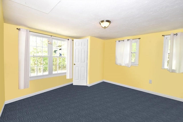 empty room featuring baseboards, dark colored carpet, and plenty of natural light