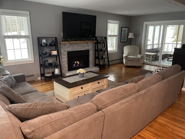 living room with a baseboard heating unit, a lit fireplace, plenty of natural light, and light wood-style floors