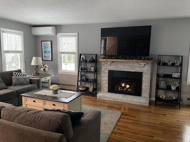 living room with a brick fireplace, plenty of natural light, wood finished floors, and a wall mounted air conditioner