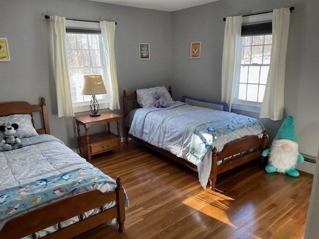 bedroom with a baseboard heating unit, multiple windows, and wood finished floors