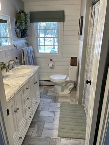 bathroom with double vanity, a baseboard radiator, a sink, and wooden walls