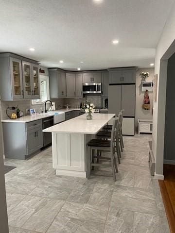 kitchen featuring stainless steel appliances, gray cabinets, light countertops, and glass insert cabinets