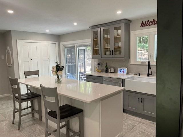 kitchen with dishwasher, a breakfast bar, a sink, and gray cabinetry