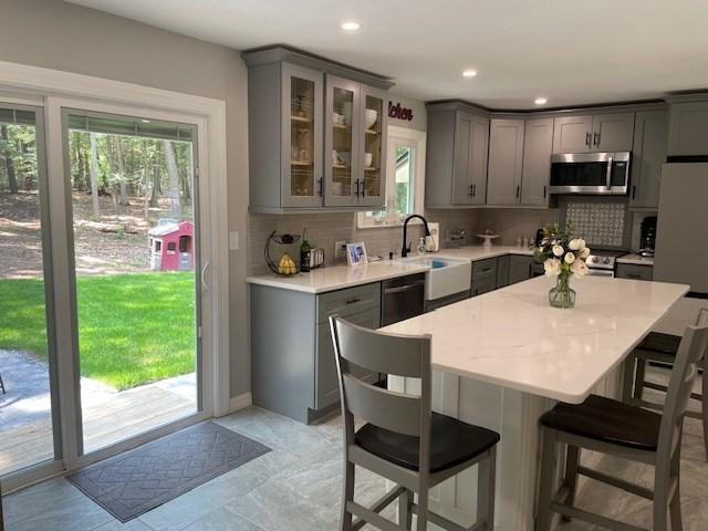 kitchen featuring appliances with stainless steel finishes, backsplash, a kitchen bar, and gray cabinetry