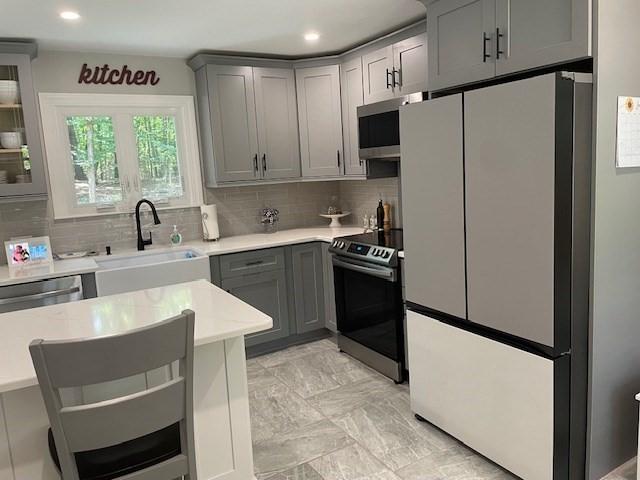 kitchen featuring tasteful backsplash, appliances with stainless steel finishes, a sink, and gray cabinetry