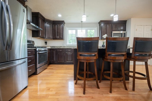 7 Willow Brook Ln, Blackstone, MA 01504 - kitchen featuring appliances with stainless steel finishes, wall chimney exhaust hood, dark brown cabinetry, light wood-type flooring, and light stone countertops