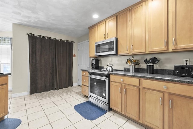 kitchen featuring light tile patterned flooring, appliances with stainless steel finishes, and dark stone counters