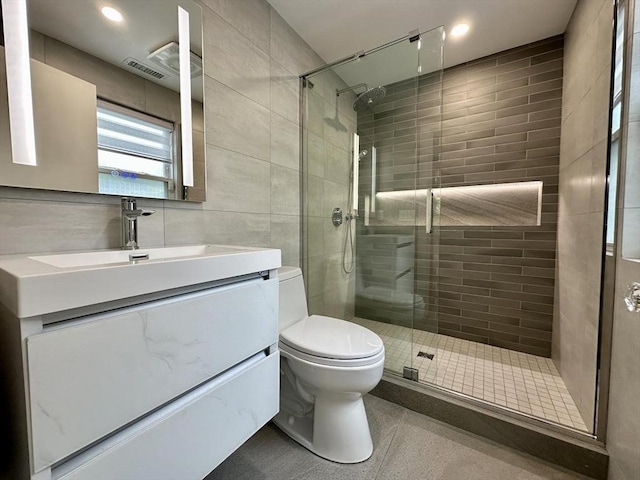 bathroom with tile walls, a stall shower, toilet, and vanity