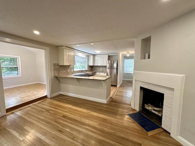 kitchen with freestanding refrigerator, a peninsula, light wood-style flooring, white cabinets, and recessed lighting