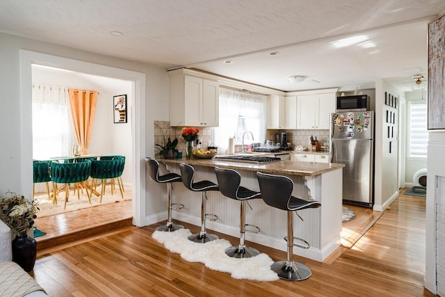 kitchen with freestanding refrigerator, white cabinetry, a peninsula, backsplash, and recessed lighting