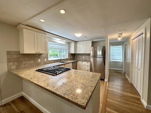 kitchen with appliances with stainless steel finishes, baseboards, a peninsula, wood finished floors, and recessed lighting