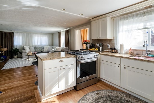 kitchen featuring gas stove, a sink, a peninsula, backsplash, and light wood-style floors