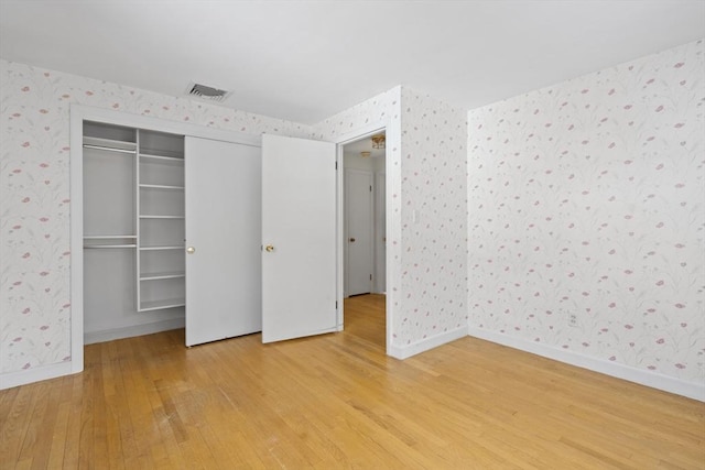 unfurnished bedroom with baseboards, wood finished floors, visible vents, and wallpapered walls