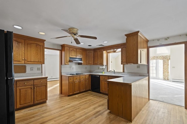 kitchen with brown cabinets, light countertops, a peninsula, under cabinet range hood, and black appliances