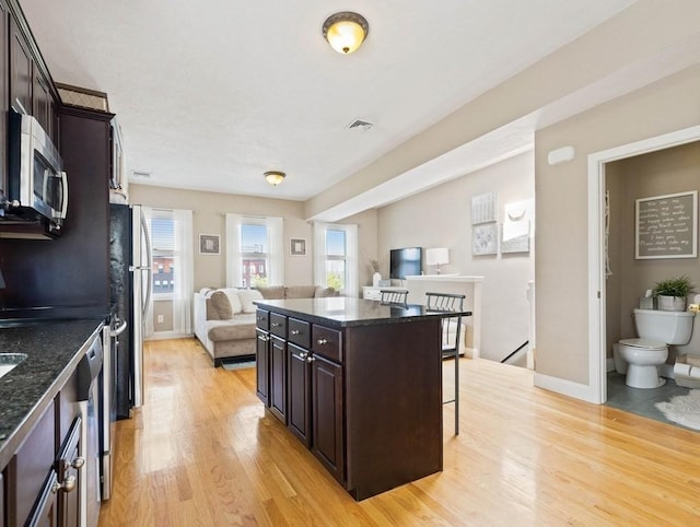 kitchen featuring light wood-type flooring, a kitchen island, dark brown cabinetry, a breakfast bar, and stainless steel appliances