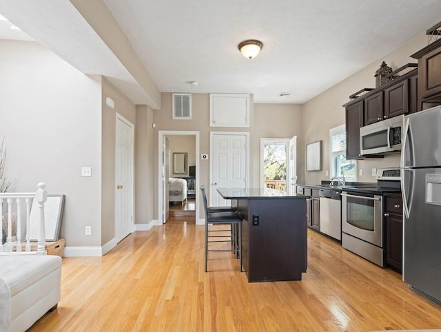 kitchen with dark brown cabinets, appliances with stainless steel finishes, light wood-type flooring, a kitchen bar, and a kitchen island