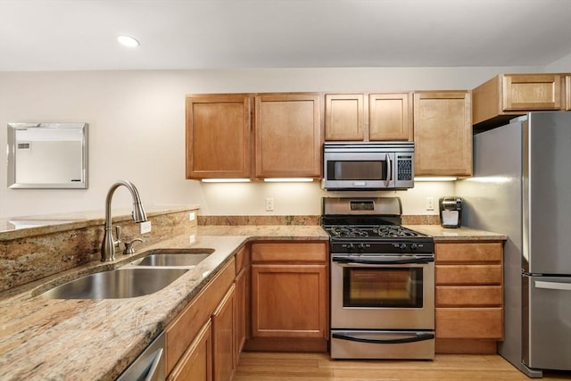 kitchen featuring light stone countertops, light wood-type flooring, recessed lighting, appliances with stainless steel finishes, and a sink