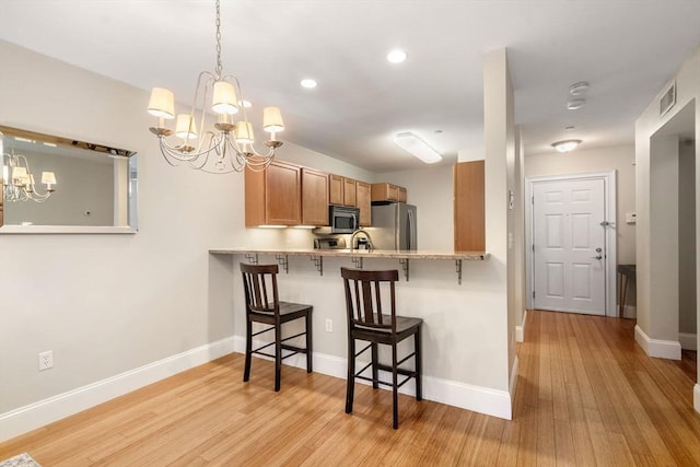 kitchen featuring a kitchen breakfast bar, appliances with stainless steel finishes, an inviting chandelier, light wood finished floors, and baseboards