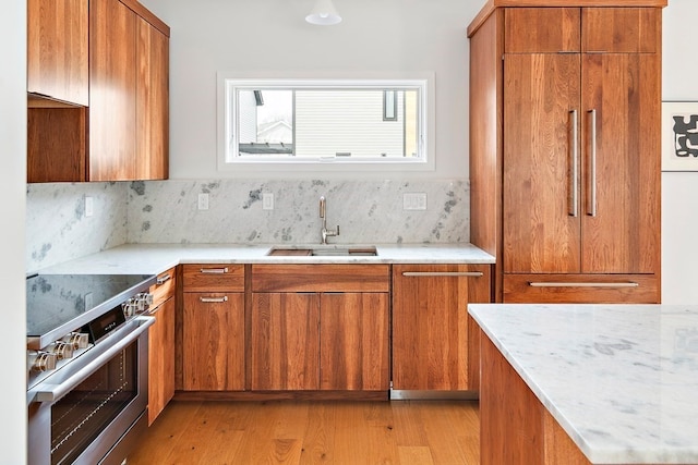 kitchen with light stone counters, sink, stainless steel range, light wood-type flooring, and decorative backsplash