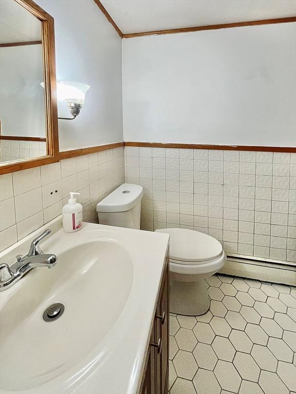 bathroom with toilet, a baseboard heating unit, tile walls, wainscoting, and vanity