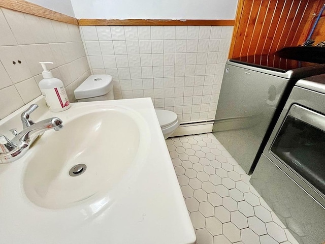 bathroom with a baseboard heating unit, tile walls, toilet, and independent washer and dryer