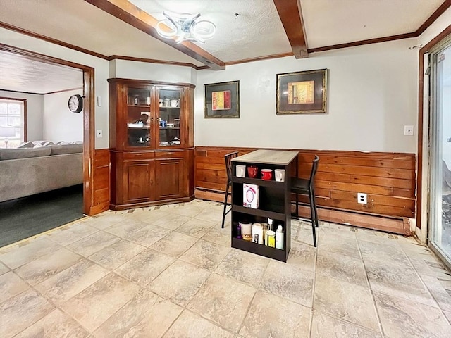 dining space with beam ceiling, wood walls, wainscoting, and crown molding