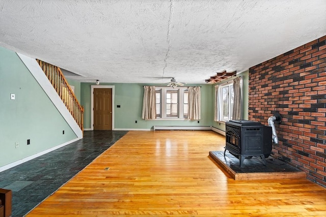 unfurnished living room with baseboards, stairway, wood finished floors, a wood stove, and a textured ceiling