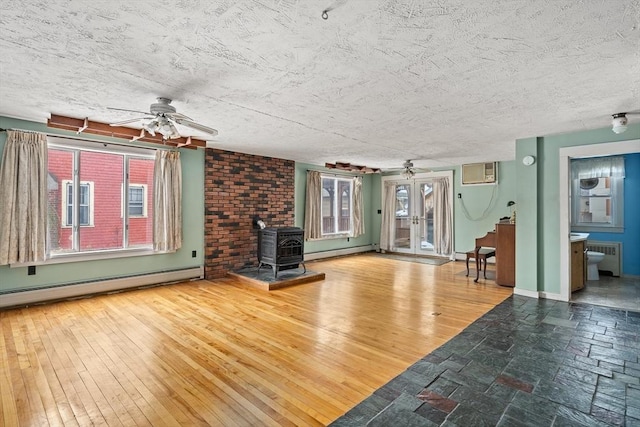 unfurnished living room with an AC wall unit, hardwood / wood-style floors, a wood stove, and baseboard heating