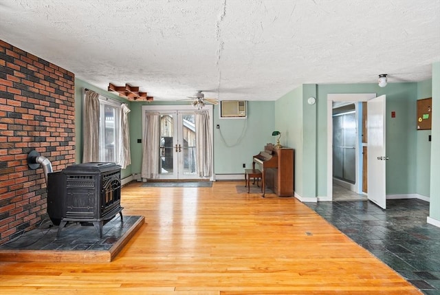 living area with a textured ceiling, wood finished floors, baseboards, french doors, and a wood stove