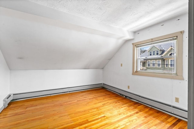 additional living space with light wood-style flooring, a baseboard heating unit, vaulted ceiling, and a textured ceiling