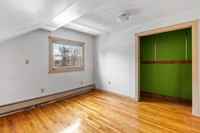 unfurnished bedroom featuring a baseboard heating unit, lofted ceiling, light wood-style floors, and a textured ceiling