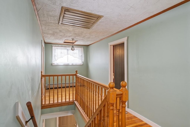 stairway with a baseboard radiator, visible vents, ornamental molding, a textured ceiling, and wood finished floors