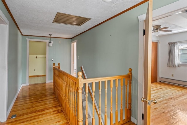 hallway featuring a baseboard heating unit, a textured ceiling, wood finished floors, and an upstairs landing