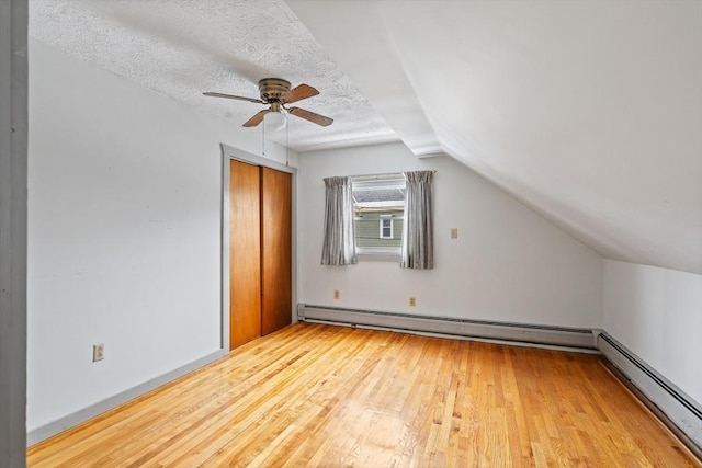 additional living space with a baseboard radiator, vaulted ceiling, a textured ceiling, and hardwood / wood-style flooring