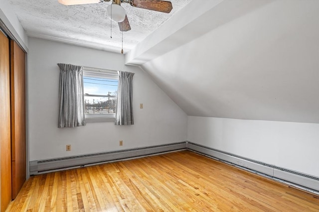 additional living space with a textured ceiling, ceiling fan, lofted ceiling, a baseboard radiator, and light wood-style flooring