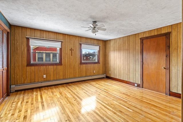 empty room with a textured ceiling, a baseboard heating unit, a ceiling fan, baseboards, and hardwood / wood-style floors