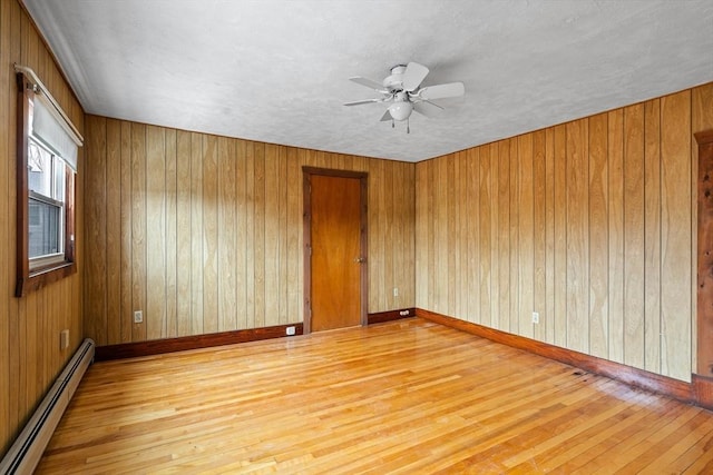 spare room with ceiling fan, a baseboard radiator, wooden walls, baseboards, and hardwood / wood-style floors