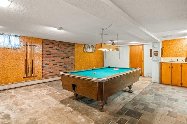 game room featuring stone finish floor, pool table, a textured ceiling, a baseboard heating unit, and a sink