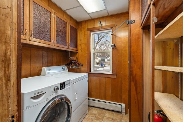 clothes washing area featuring wood walls, a baseboard radiator, cabinet space, and washing machine and clothes dryer