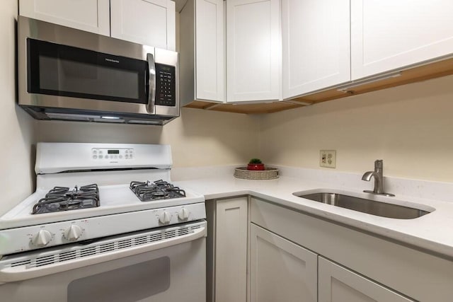 kitchen featuring white gas range, white cabinets, stainless steel microwave, and a sink