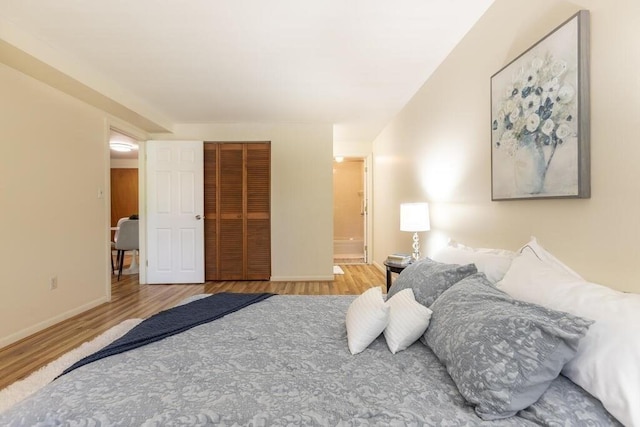 bedroom featuring a closet, baseboards, ensuite bathroom, and wood finished floors