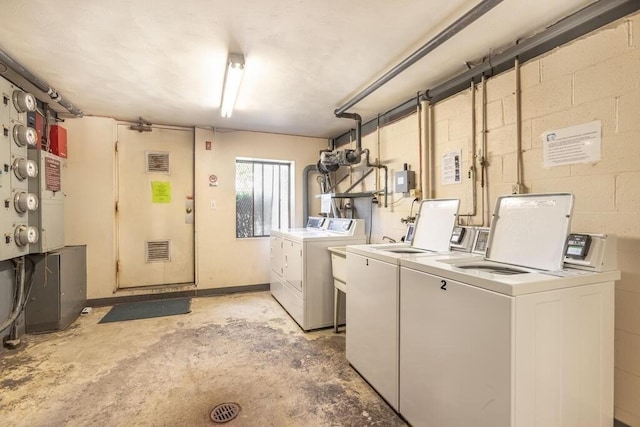 community laundry room featuring washer and dryer, concrete block wall, and visible vents