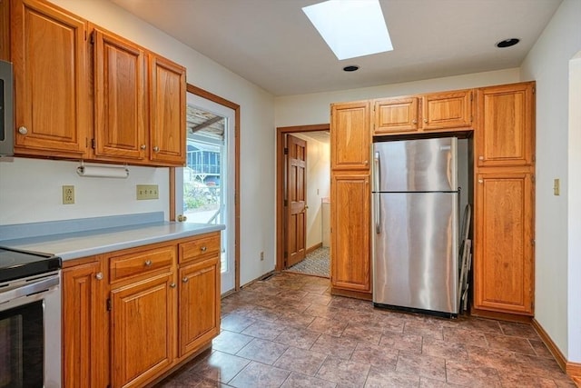 kitchen featuring stainless steel appliances, a skylight, baseboards, light countertops, and brown cabinets