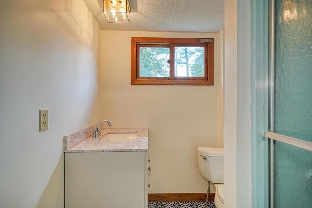 bathroom with a textured ceiling, vanity, toilet, and baseboards