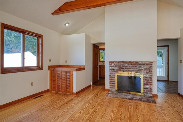 unfurnished living room with light wood-style flooring, a brick fireplace, high vaulted ceiling, beamed ceiling, and baseboards